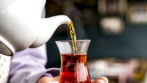 side-view-person-pouring-black-tea-from-white-ceramic-teapot-into-armudu-glass-1.webp